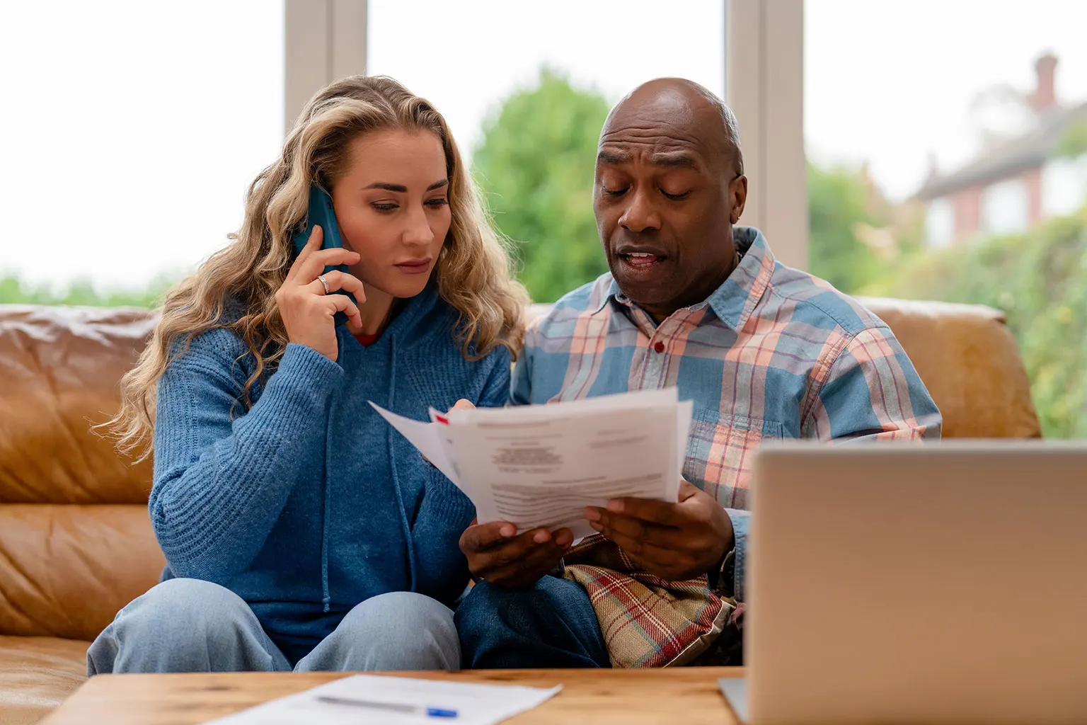 Two people reviewing paperwork on a sofa, with one holding a phone to her ear.