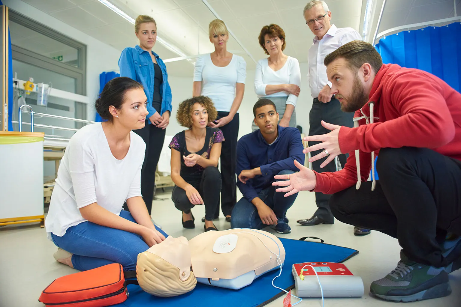 A group practising first aid with a training manikin and a defibrillator.