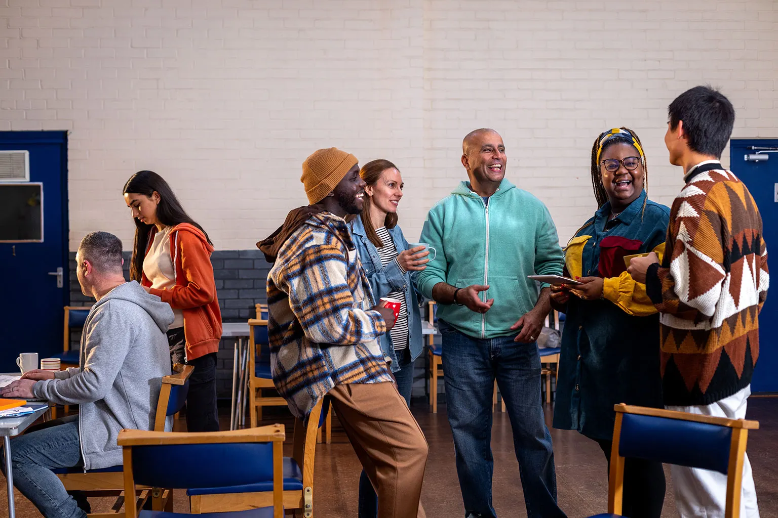 People talking together in a community hall with tables and chairs.