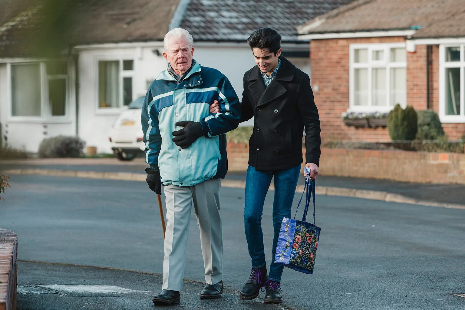 Two people walking arm in arm outdoors, one using a walking stick.